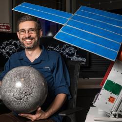 Craig Hardgrove holds a globe of the moon with a full size model of LunaH-Map beside him.