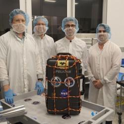 Four individuals in full clean room bunny suits stand in front of a suitcase that contain the LunaH-Map instrument.